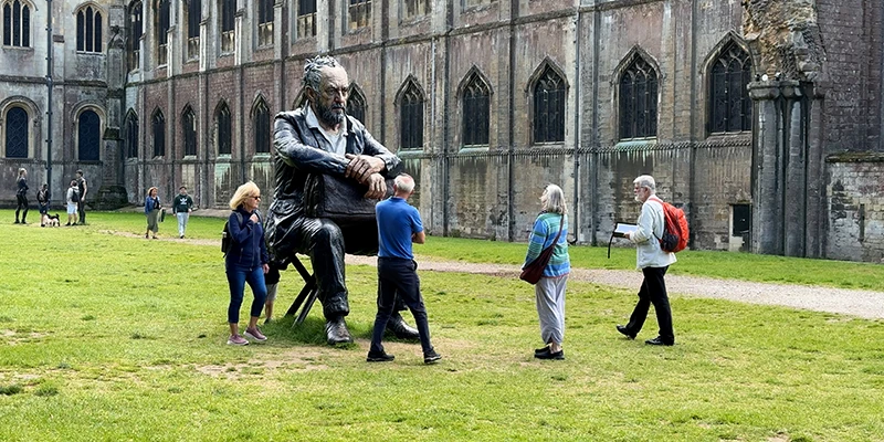 A seated bronze figure by Sean Henry on the green beside Ely Cathedral