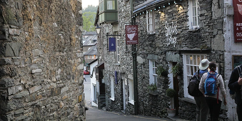 Walkers with rucksacks on a narrow stone-walled lane in Ambleside