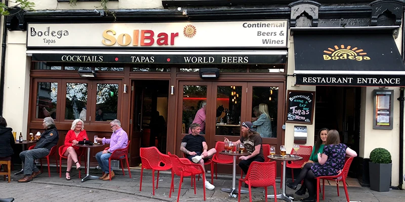 Diners at outdoor tables with red chairs in Bowness