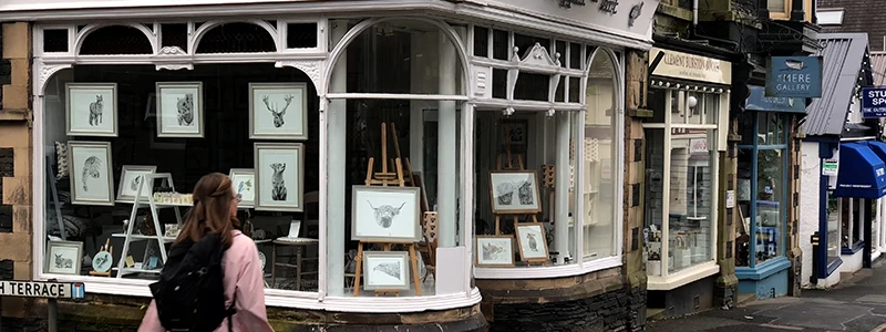 Visitor looking at framed prints in the window of a Windermere art gallery