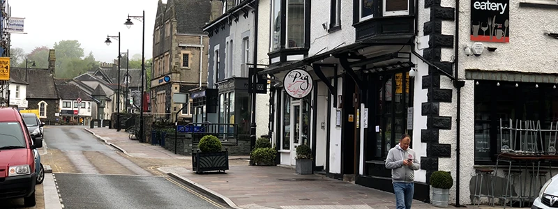 Main street in Windermere town with stone shopfronts and a pedestrian on the sidewalk