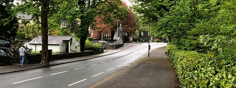 Tree-lined road between Windermere and Bowness with a walker on the sidewalk