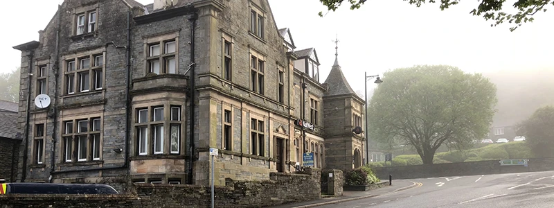 Large Victorian stone hotel with a corner turret seen through morning fog in Windermere