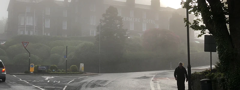 Misty road on the edge of Windermere with a walker under bare trees