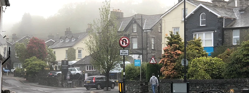 Foggy street in Windermere sloping downhill past stone houses and parked cars