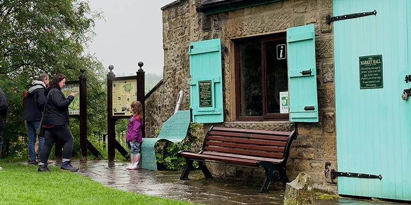 A shop with bright turquoise shutters and a bench in Eyam