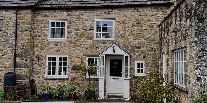 A stone cottage with a white door and flower boxes in Eyam