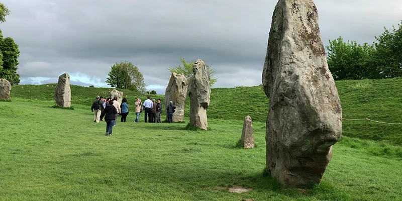 A tall standing stone at Avebury with visitors alongside