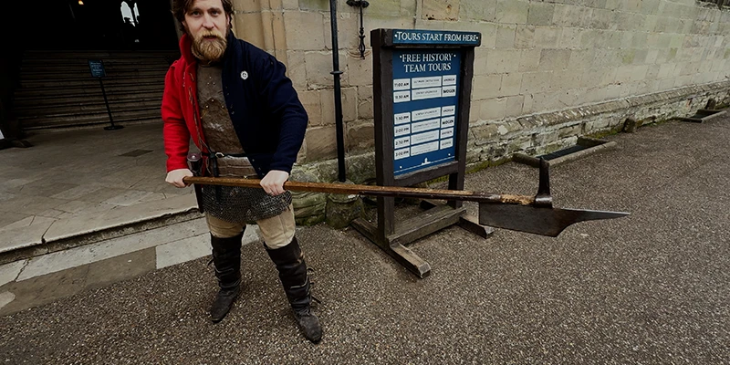 Castle guide demonstrating a medieval bill, a farm tool adapted as a weapon
