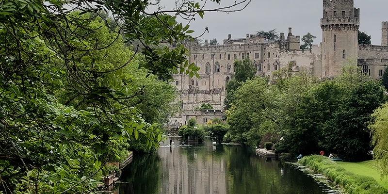 Warwick Castle towers seen from the River Avon with boats on the water