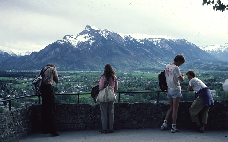 Visitors at a viewpoint above Salzburg looking toward snow-capped mountains