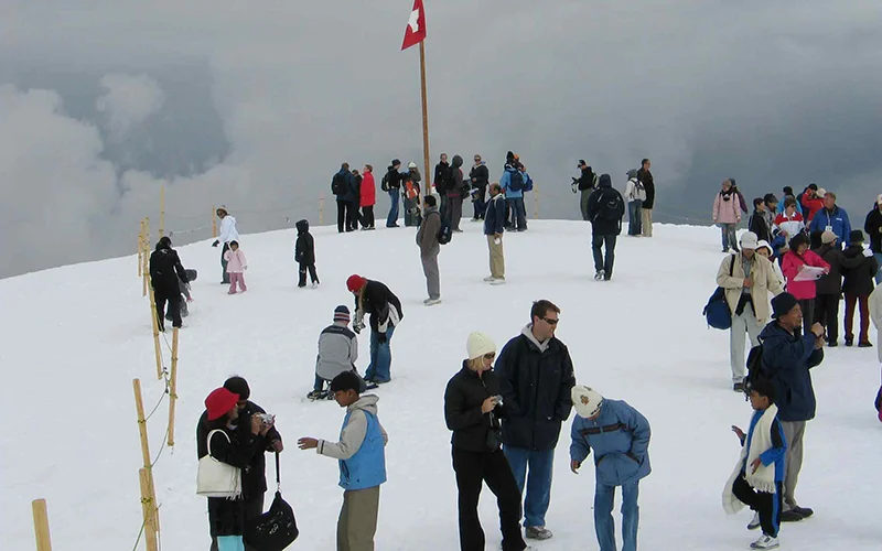 Visitors walking on the snow at the Jungfraujoch with a Swiss flag