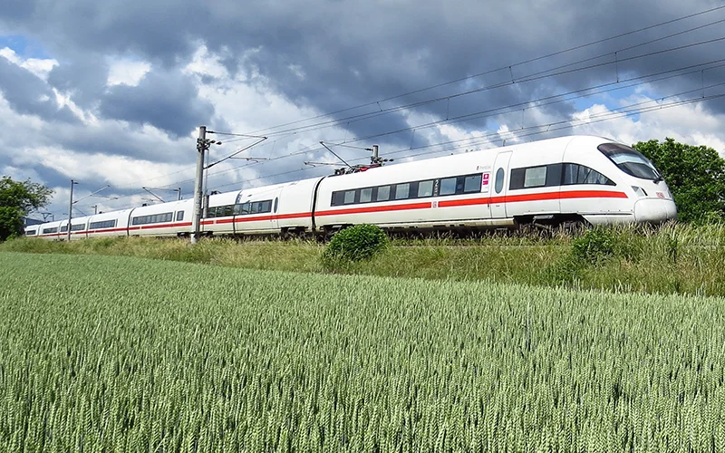 High-speed white and red train running past a green field in Europe