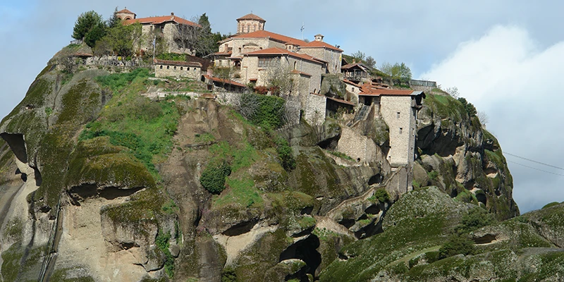 Meteora monastery with red roofs above the green hillside